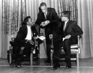 This is a October 30, 1961 photo of Bayard Rustin (seated left) and Malcolm X (standing) at their Howard University debate. Seated to the right is Michael Winston, the debate moderator. (Photo Credit: AP / John Duricka)